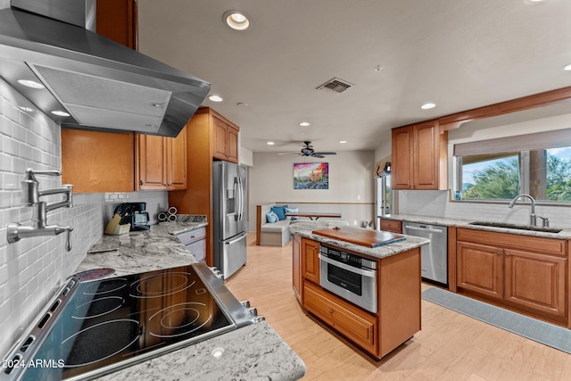 kitchen with appliances with stainless steel finishes, light stone counters, ventilation hood, sink, and a kitchen island