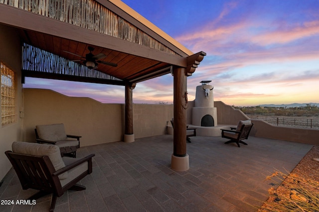 patio terrace at dusk featuring ceiling fan and an outdoor fireplace