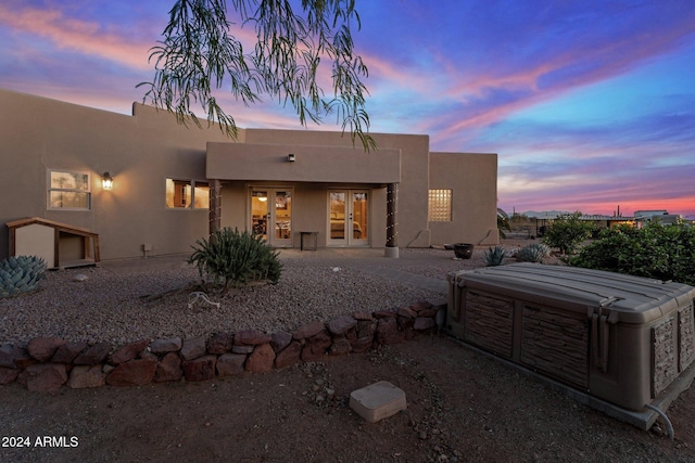 back house at dusk featuring french doors and a hot tub