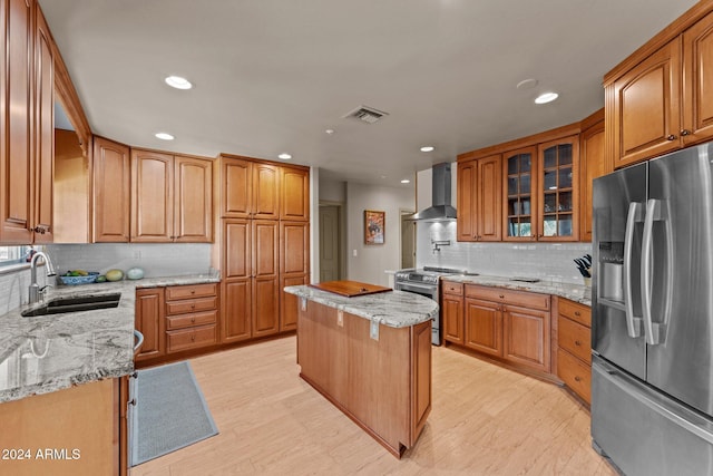 kitchen featuring sink, wall chimney range hood, light stone counters, a kitchen island, and appliances with stainless steel finishes