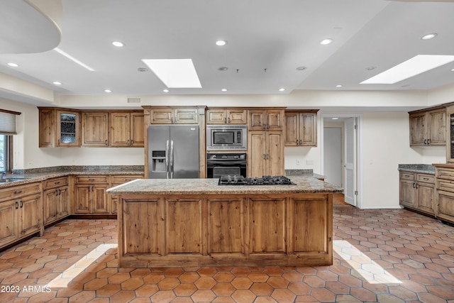 kitchen featuring light stone counters, a skylight, a center island, and black appliances