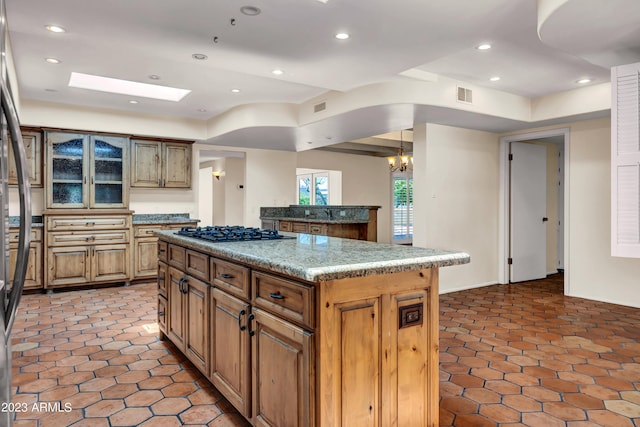 kitchen with a skylight, a center island, a notable chandelier, black gas cooktop, and light stone countertops