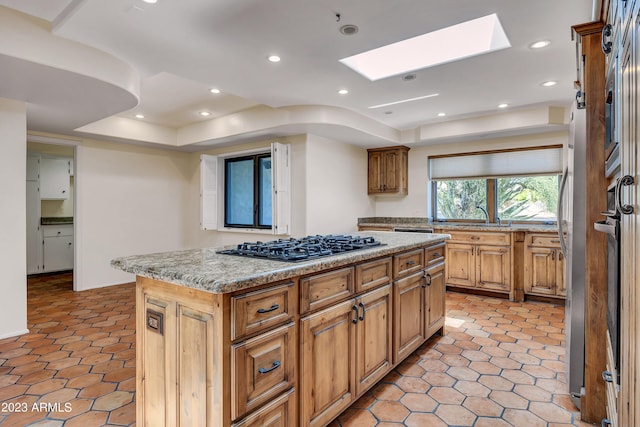 kitchen featuring a skylight, light stone counters, a kitchen island, black gas stovetop, and a raised ceiling