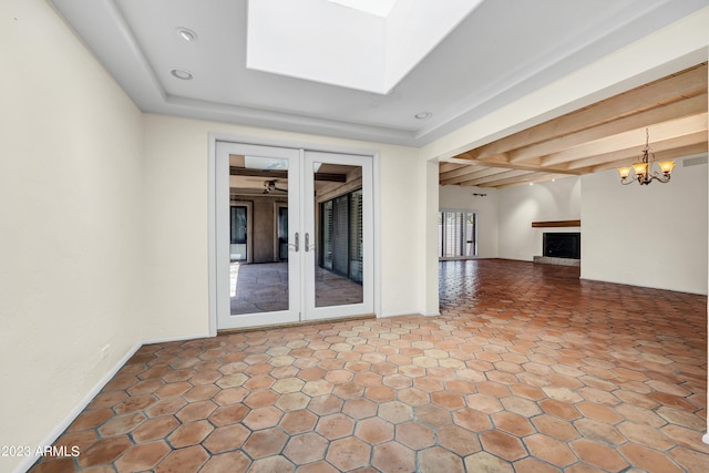 unfurnished living room featuring a chandelier, beam ceiling, and french doors