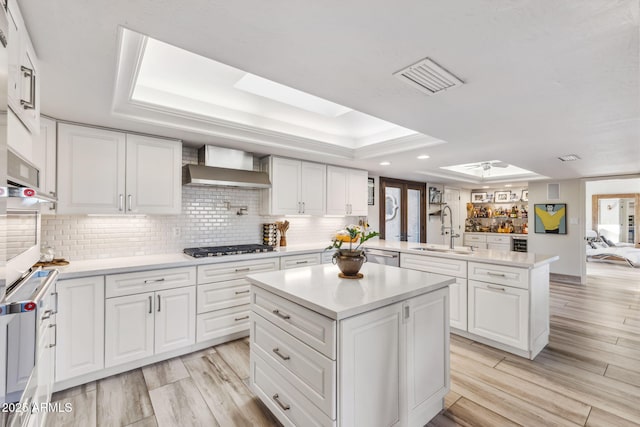 kitchen featuring a kitchen island, a skylight, sink, kitchen peninsula, and wall chimney exhaust hood