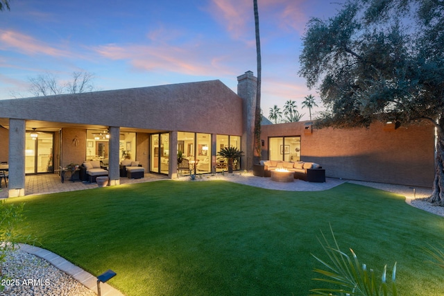 back house at dusk featuring a yard, a patio, and an outdoor living space with a fire pit