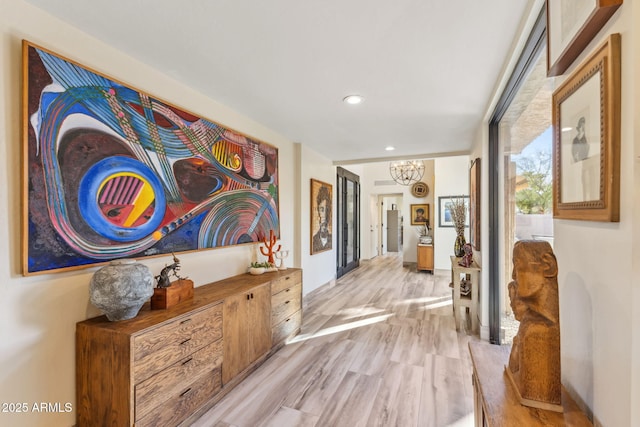 corridor featuring an inviting chandelier and light hardwood / wood-style flooring