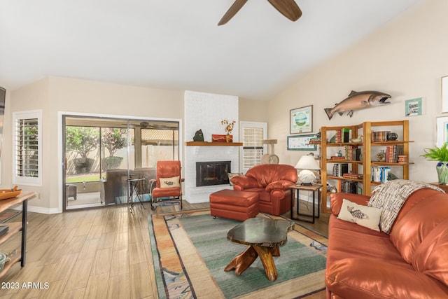 living room with lofted ceiling, a brick fireplace, ceiling fan, and light wood-type flooring