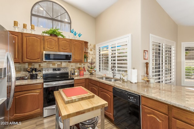 kitchen featuring sink, light stone counters, light hardwood / wood-style flooring, appliances with stainless steel finishes, and decorative backsplash