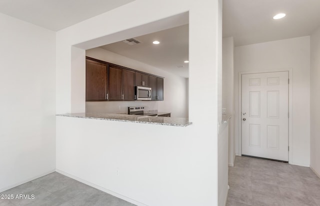 kitchen featuring appliances with stainless steel finishes, dark brown cabinetry, light stone countertops, and kitchen peninsula