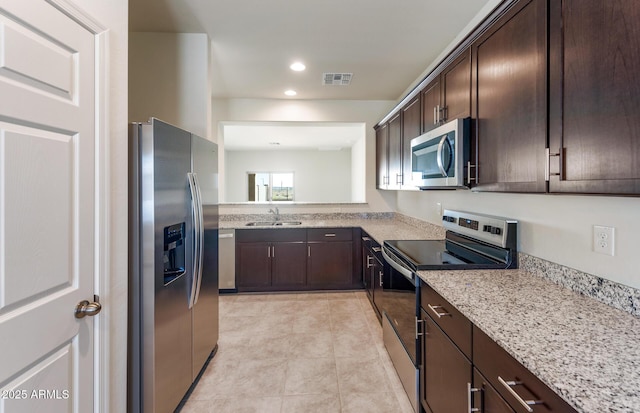 kitchen featuring light stone countertops, sink, dark brown cabinets, light tile patterned floors, and appliances with stainless steel finishes