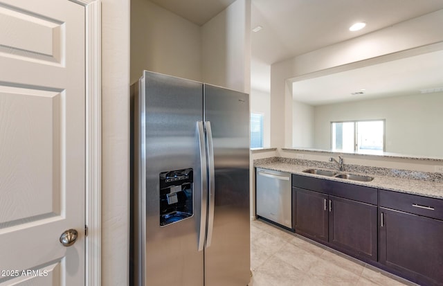 kitchen featuring sink, dark brown cabinets, light stone counters, light tile patterned floors, and appliances with stainless steel finishes