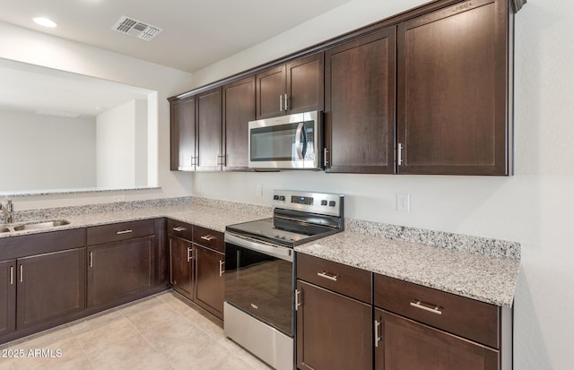 kitchen with appliances with stainless steel finishes, dark brown cabinetry, light stone counters, light tile patterned floors, and sink