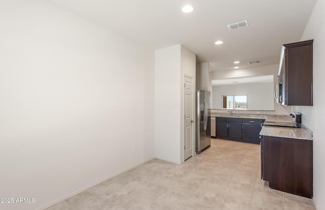 kitchen featuring sink, appliances with stainless steel finishes, dark brown cabinets, and light stone countertops