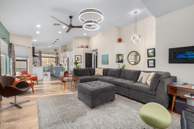 living room featuring ceiling fan, a towering ceiling, and light hardwood / wood-style floors