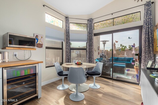 dining area with light hardwood / wood-style flooring, beverage cooler, and lofted ceiling