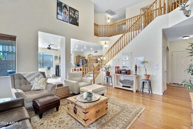 living room featuring light hardwood / wood-style flooring, a towering ceiling, and ceiling fan