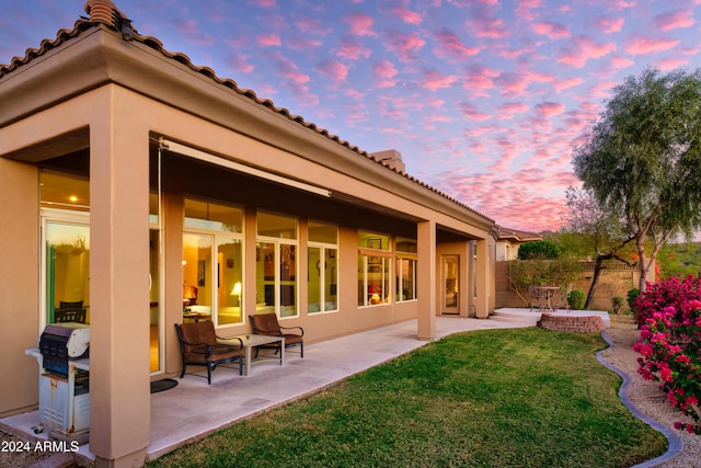 back house at dusk with a lawn and a patio