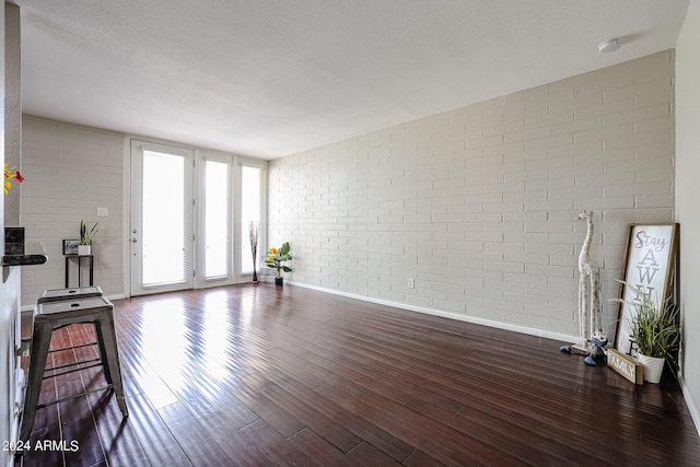 unfurnished living room featuring a textured ceiling, dark hardwood / wood-style floors, and brick wall