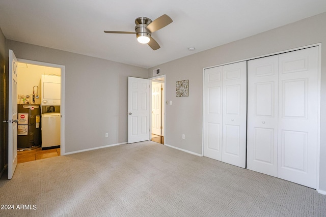 unfurnished bedroom with light colored carpet, ceiling fan, water heater, stacked washer and dryer, and a closet