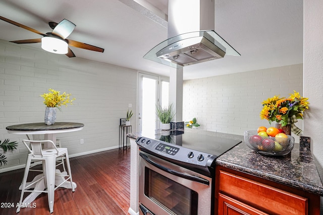 kitchen featuring stainless steel range with electric stovetop, brick wall, island range hood, dark wood-type flooring, and dark stone countertops