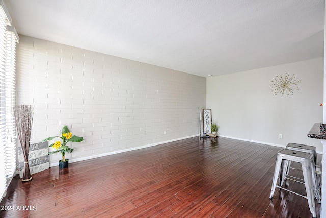 living room with a textured ceiling, dark hardwood / wood-style floors, and brick wall