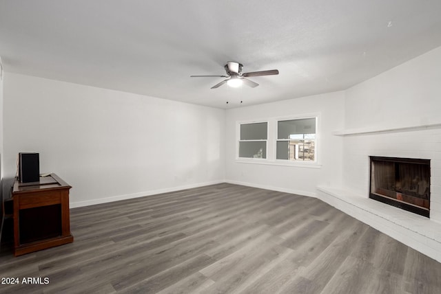 unfurnished living room featuring ceiling fan, wood-type flooring, and a brick fireplace