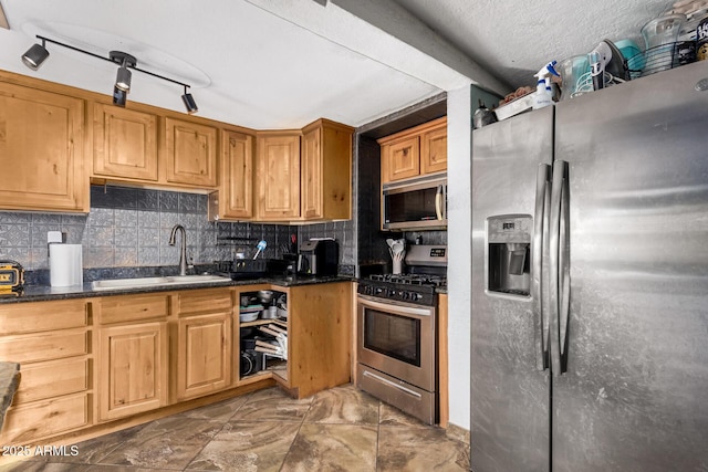 kitchen with sink, dark stone counters, track lighting, stainless steel appliances, and decorative backsplash