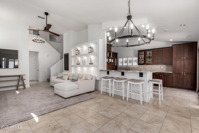 9100 E Captain Dreyfus Ave, Scottsdale, AZ 85260 - kitchen featuring a chandelier, a kitchen bar, dark brown cabinetry, ceiling fan, and glass insert cabinets