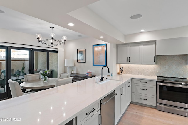 kitchen featuring sink, light stone counters, hanging light fixtures, appliances with stainless steel finishes, and backsplash