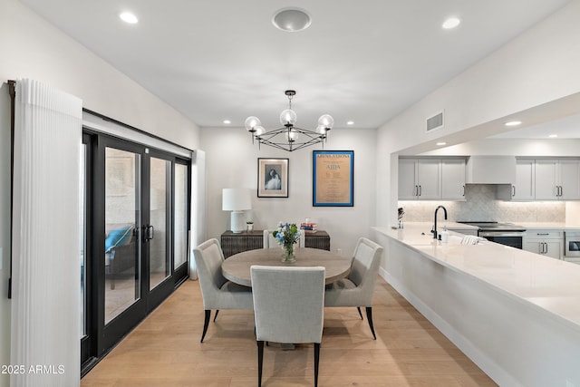 dining area featuring french doors, a notable chandelier, sink, and light wood-type flooring