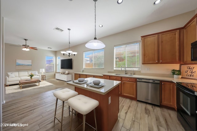 kitchen with a kitchen bar, light hardwood / wood-style floors, black appliances, sink, and pendant lighting