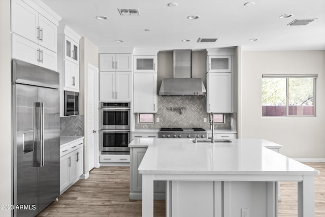 kitchen featuring a center island with sink, wall chimney exhaust hood, stainless steel appliances, and a breakfast bar area