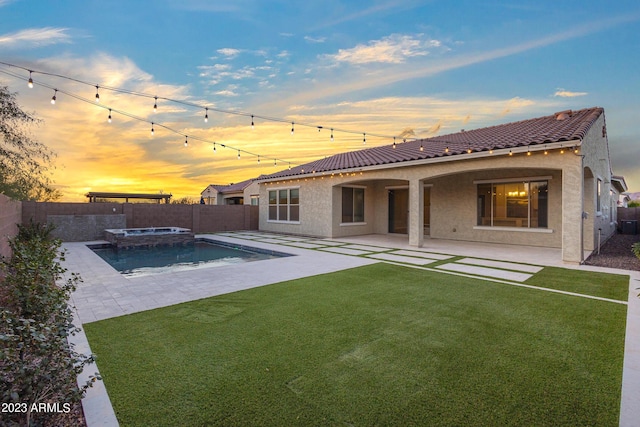 back house at dusk featuring a patio area, a yard, and a pool with hot tub