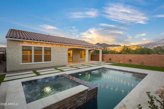 pool at dusk with an in ground hot tub and a patio