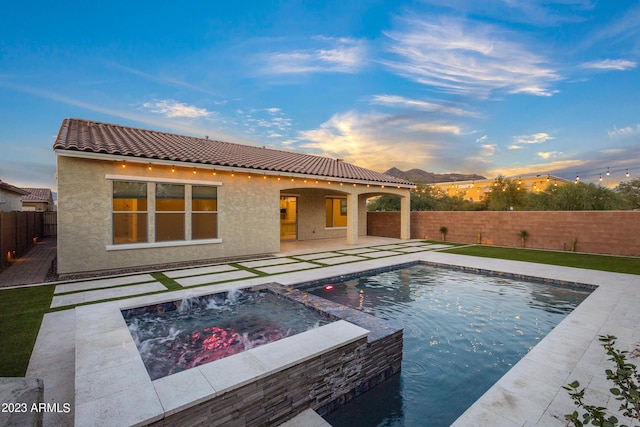 pool at dusk featuring a patio area and an in ground hot tub