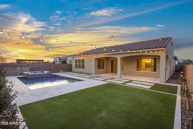 back house at dusk featuring a lawn, a patio area, and a swimming pool with hot tub