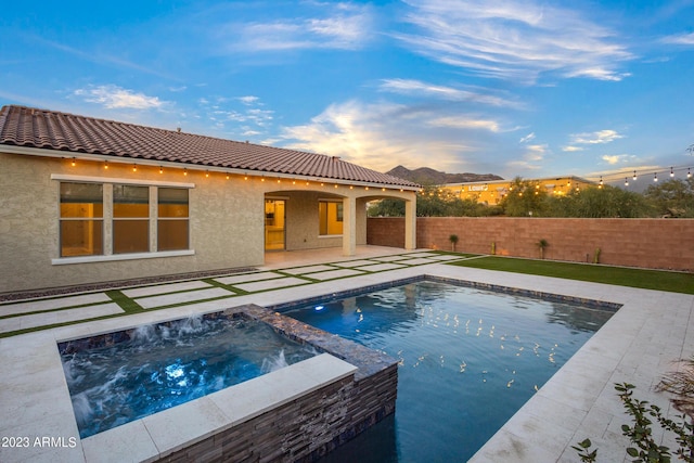 pool at dusk featuring an in ground hot tub