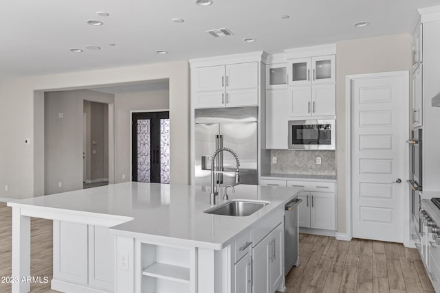 kitchen with tasteful backsplash, a kitchen island with sink, sink, built in appliances, and white cabinetry