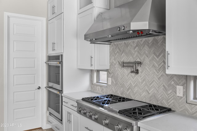 kitchen with white cabinets, wall chimney range hood, stainless steel appliances, and tasteful backsplash