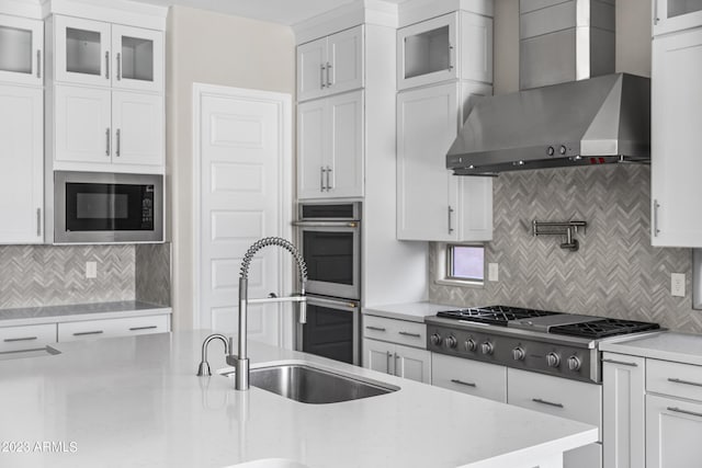 kitchen featuring white cabinets, wall chimney exhaust hood, decorative backsplash, and appliances with stainless steel finishes