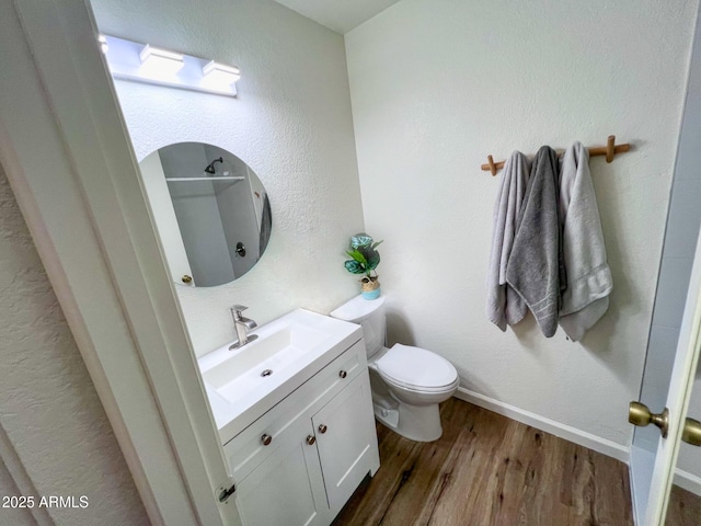 bathroom featuring baseboards, a textured wall, toilet, wood finished floors, and vanity