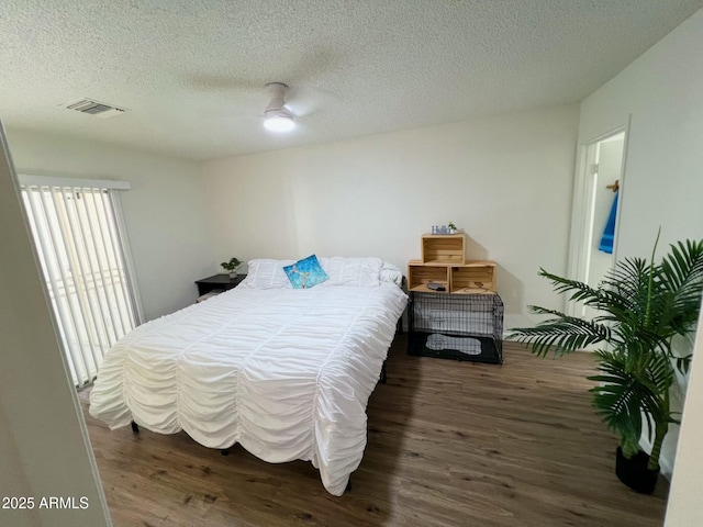 bedroom featuring dark wood-style floors, visible vents, a textured ceiling, and a ceiling fan