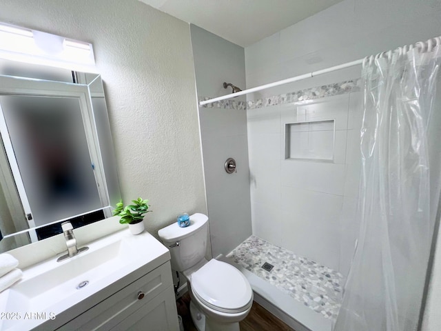 full bathroom featuring a shower stall, a textured wall, vanity, and toilet