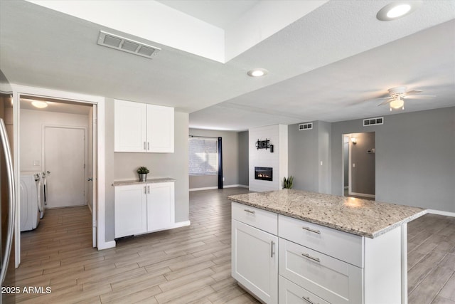 kitchen with a fireplace, white cabinetry, a center island, light stone counters, and ceiling fan