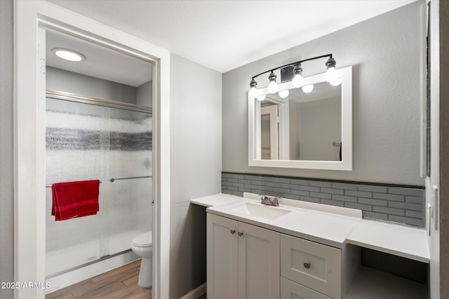 bathroom featuring walk in shower, toilet, vanity, hardwood / wood-style floors, and backsplash