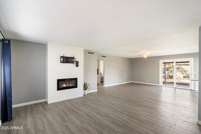 unfurnished living room with hardwood / wood-style flooring, a large fireplace, and ceiling fan