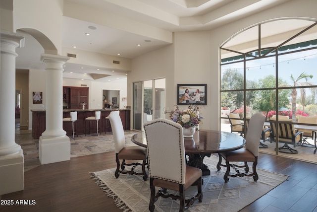 dining area with ornate columns, a high ceiling, visible vents, and wood finished floors