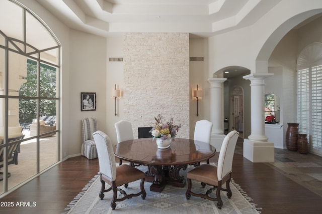 dining room with arched walkways, decorative columns, wood finished floors, and a towering ceiling