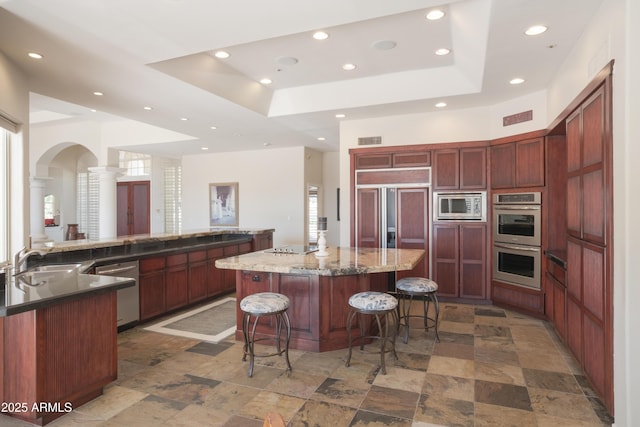 kitchen featuring decorative columns, built in appliances, a spacious island, recessed lighting, and a sink